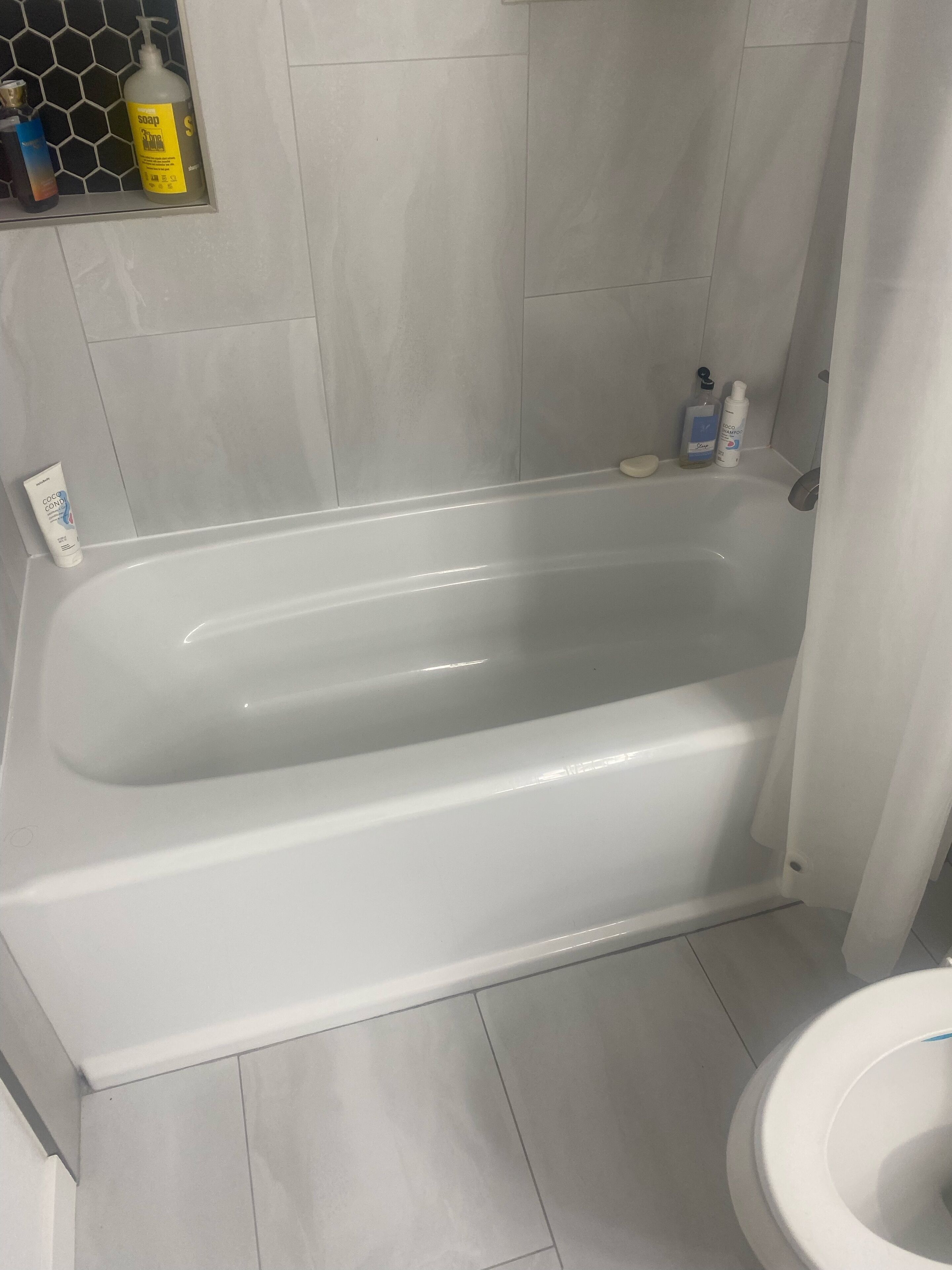 Une salle de bain avec une baignoire blanche, des toilettes et divers produits de toilette rangés sur une étagère.