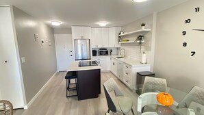 A modern kitchen with white cabinets, a stainless steel refrigerator, and a glass dining table with chairs. - Lovely 1-bedroom condo near shops & dining! (Denver)