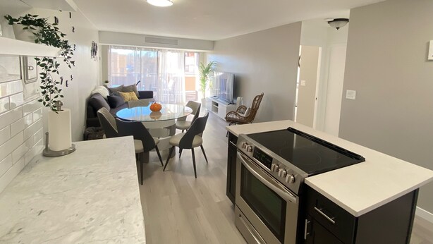 A modern kitchen with a central island, a built-in oven, and a dining area with a round table and chairs. - Lovely 1-bedroom condo near shops & dining! (Denver)