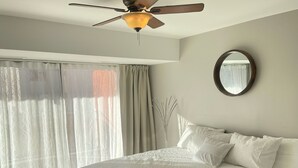 A bedroom with a bed, a ceiling fan, a window with curtains, and a round mirror on the wall. - Lovely 1-bedroom condo near shops & dining! (Denver)
