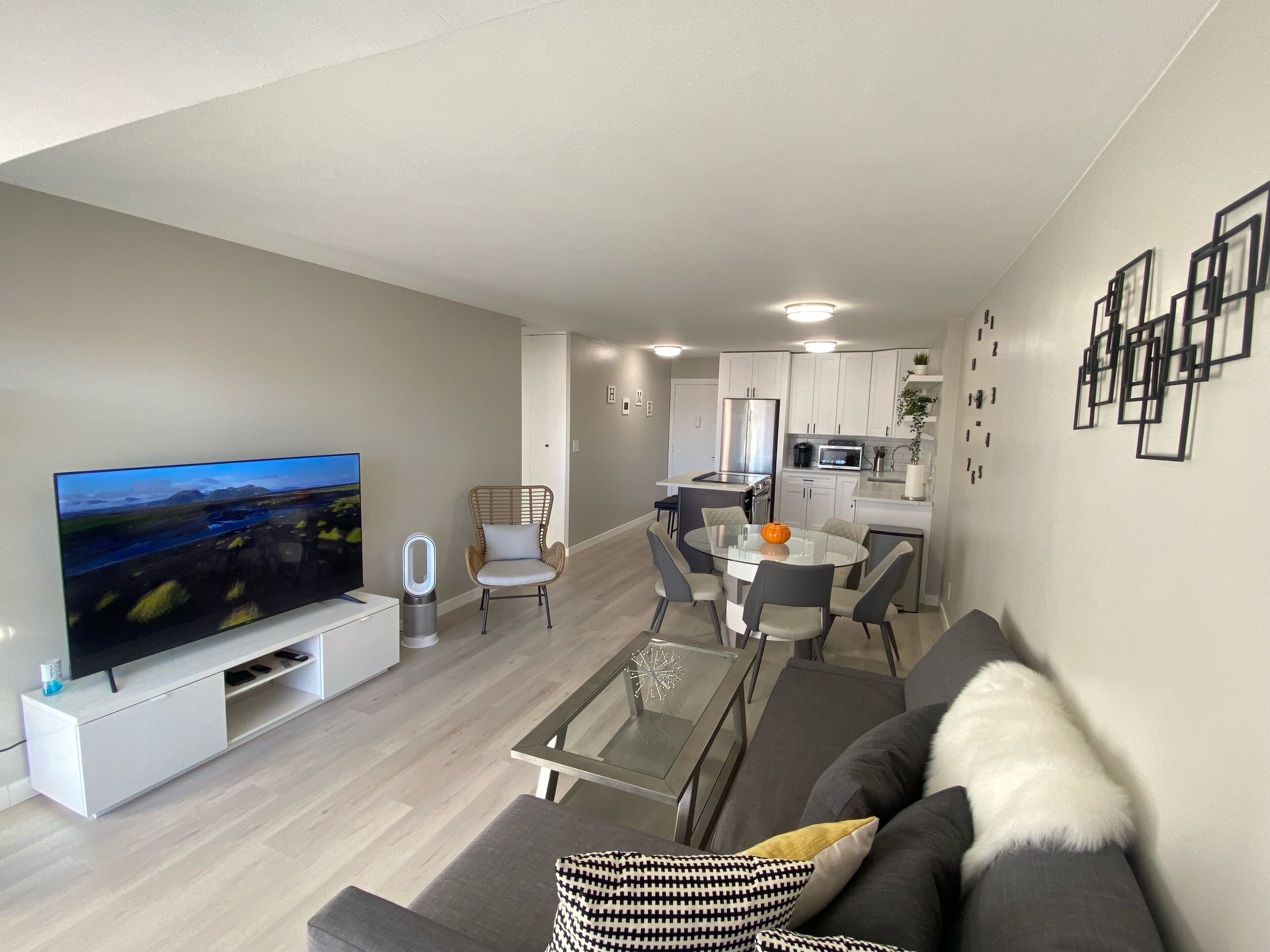 Uma sala de estar moderna com uma televisão de tela plana, uma mesa de centro de vidro e um sofá cinza.