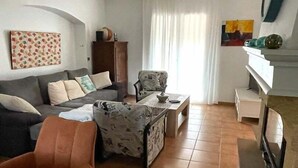 Een woonkamer met een bank, fauteuils, een salontafel, een televisie en een open haard.