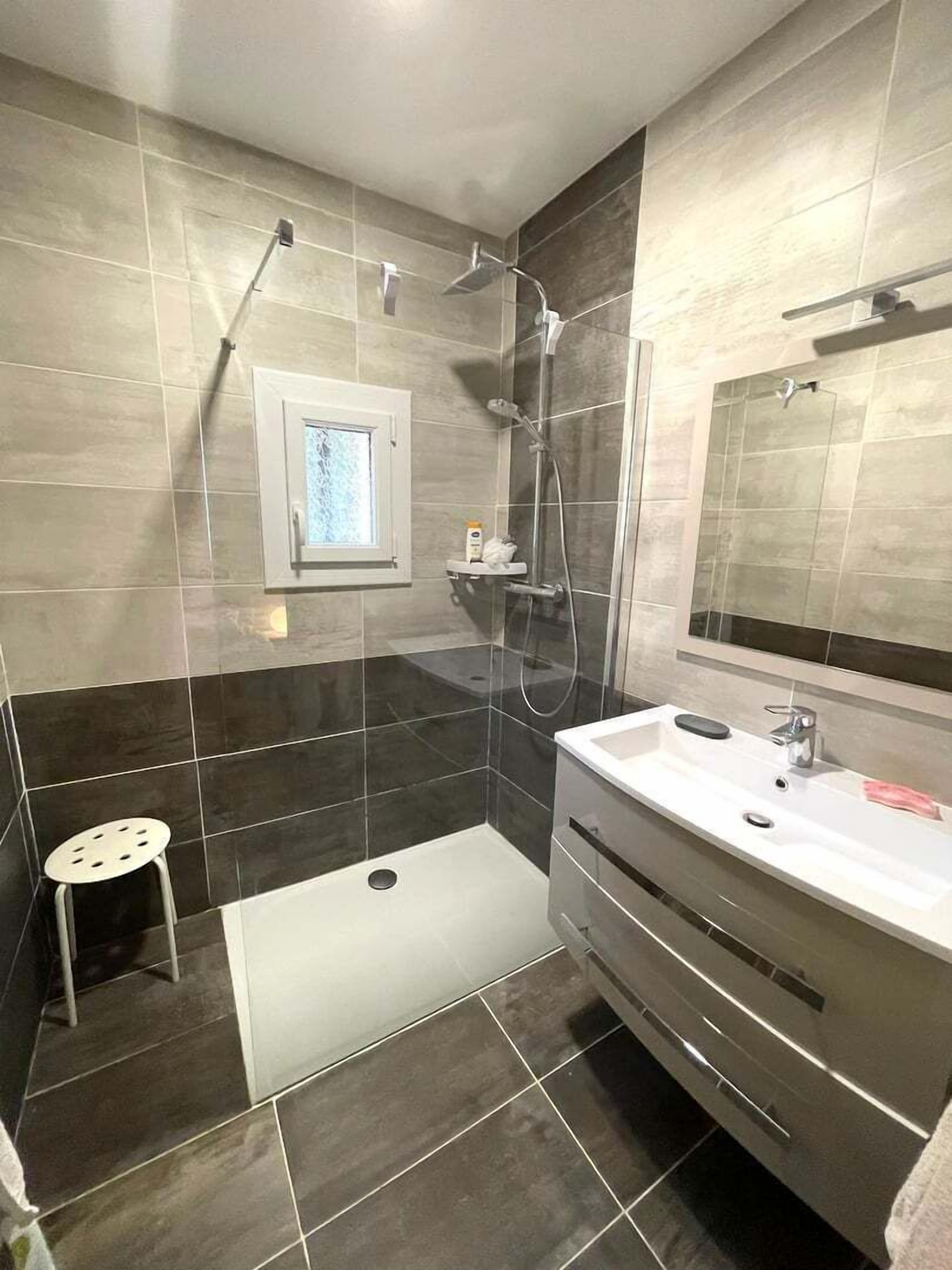 Ein modernes Badezimmer mit Dusche, Waschbecken und einem kleinen Hocker.