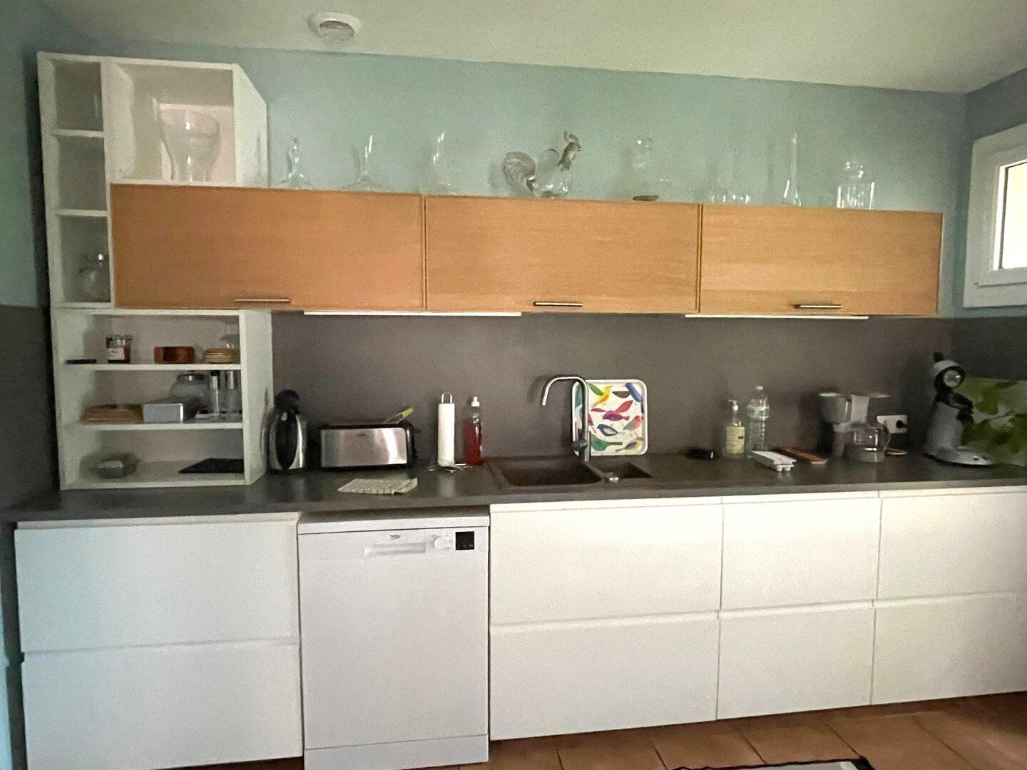 A kitchen with white cabinets, a dishwasher, a toaster, and various kitchen items on the countertop.