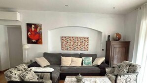 Een woonkamer met een grijze bank, een wandkleed met patroon en een kast.