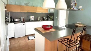 Een moderne keuken met witte kastjes, een inbouwvaatwasser, een rode kom op het eiland en hangende lampen.