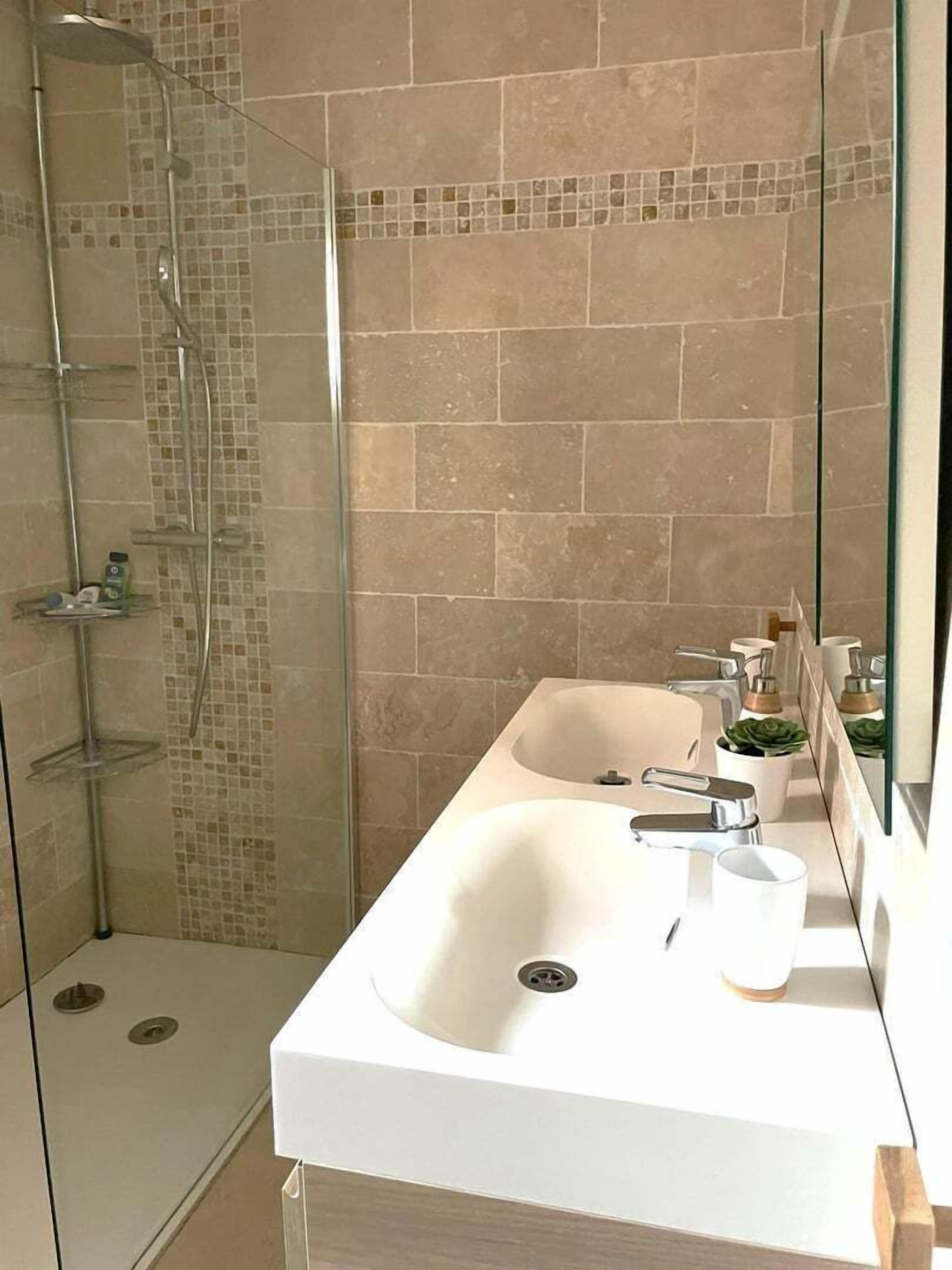 A modern bathroom with a glass shower enclosure, a white sink with a mirror, and a tiled backsplash.