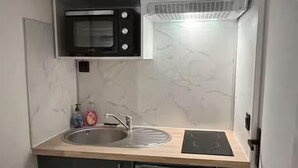 A compact kitchen with a built-in microwave, oven, and refrigerator, a sink with a faucet, and a lighted countertop. - L’Hermione – city center & thermal baths (Rochefort)