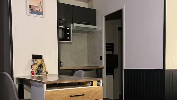 A compact kitchen with a microwave, a small refrigerator, and a wooden cabinet with drawers. - L’Hermione – city center & thermal baths (Rochefort)
