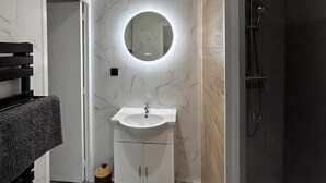 A modern bathroom with a marble vanity, a round mirror, a shower, and a wooden floor. - L’Hermione – city center & thermal baths (Rochefort)