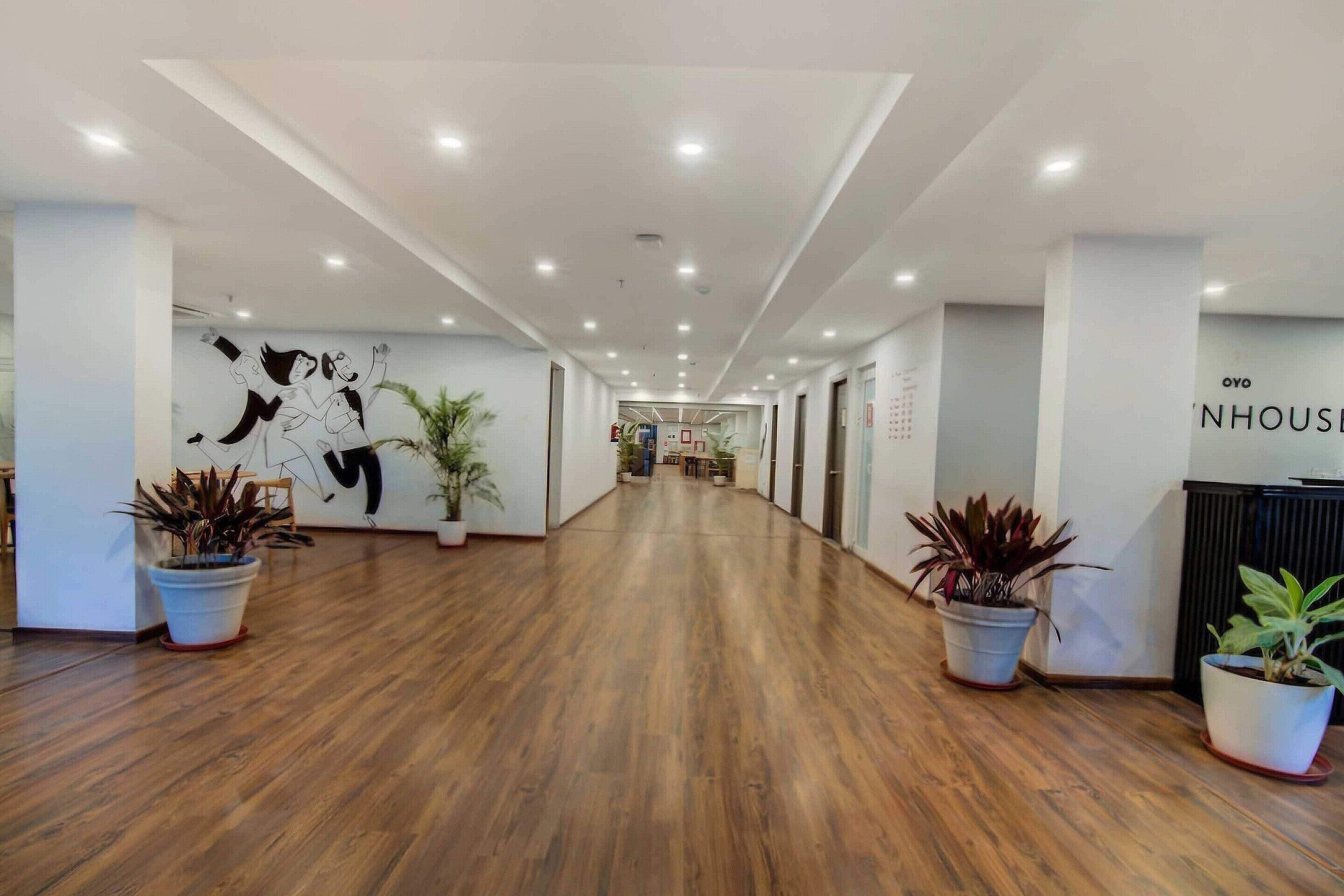 A hotel corridor with wooden flooring, potted plants, and a wall with abstract art.