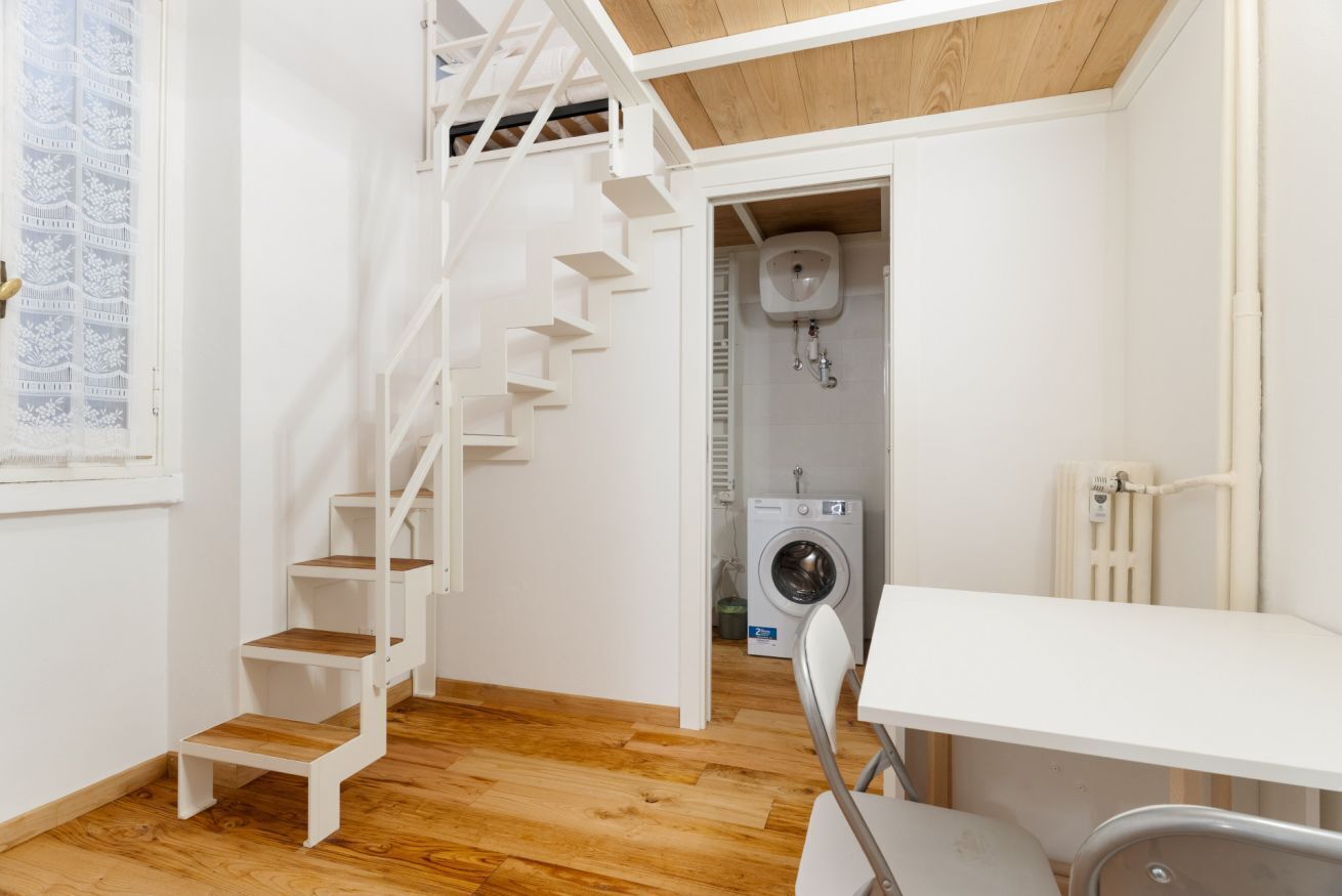 A compact room with a white staircase, a washing machine, and a radiator.