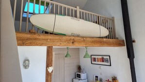 Un dormitorio tipo loft con techo blanco, vigas de madera, una tabla de surf y una tubería negra.