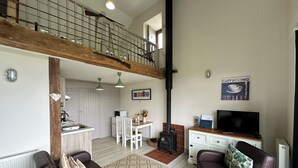 Un salón espacioso con techo alto, una cocina al fondo y una zona de estar acogedora con sofás de cuero y chimenea.