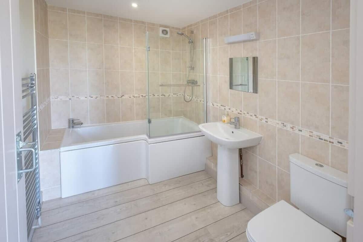 Een moderne badkamer met een douche in een glazen cabine, een vrijstaand bad, een wastafel op een zuil en een toilet.