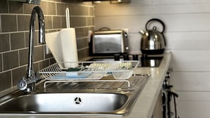 Una cocina moderna con un lavamanos de acero inoxidable, un escurreplatos, una tetera y un tostador.