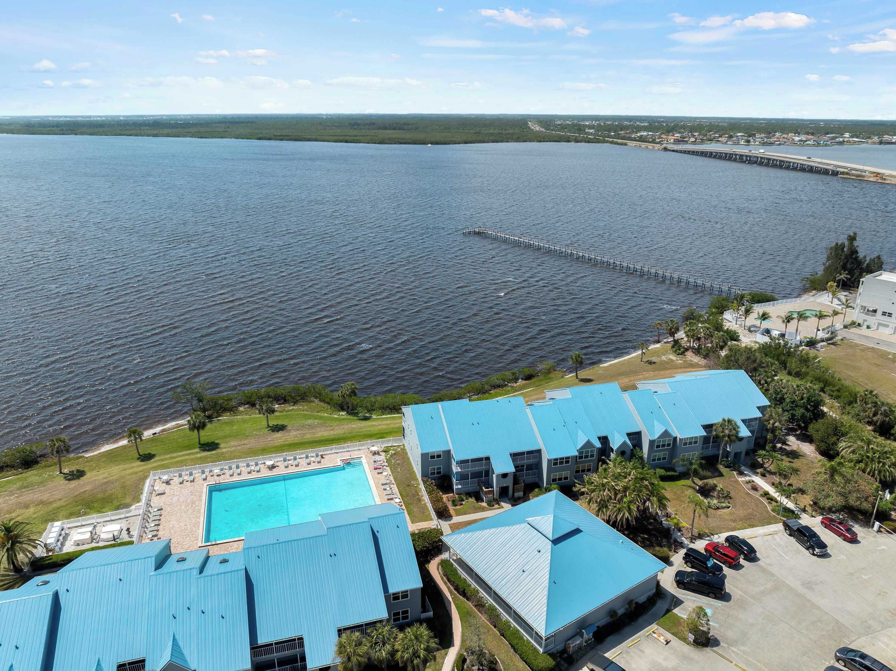 Um resort com uma piscina grande, vários edifícios com telhados azuis e vista para a água.