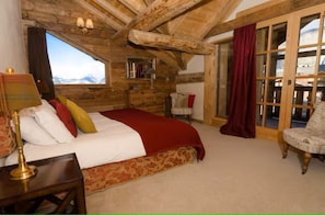 Ein Schlafzimmer mit einem großen Bett, Holzboden, einem Fenster mit Bergblick und einem roten Vorhang.