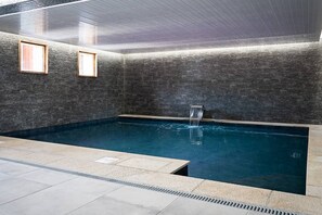 An indoor swimming pool with a stone wall, a water feature, and two framed pictures on the wall. - Presidential Suite (Sainte-Foy-Tarentaise)