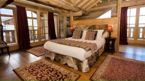 A spacious bedroom with a large bed, wooden beams, and a view through large windows. - Presidential Suite (Sainte-Foy-Tarentaise)