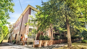 Un edificio de varios pisos de ladrillo con un espacio exterior cubierto, una señal de no estacionamiento y una calle bordeada de árboles.