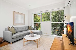 A living room with a grey sofa, a round coffee table, a framed picture on the wall, and a TV on a wooden stand. - Bright 2-bed Apartment in South Yarra (Melbourne)
