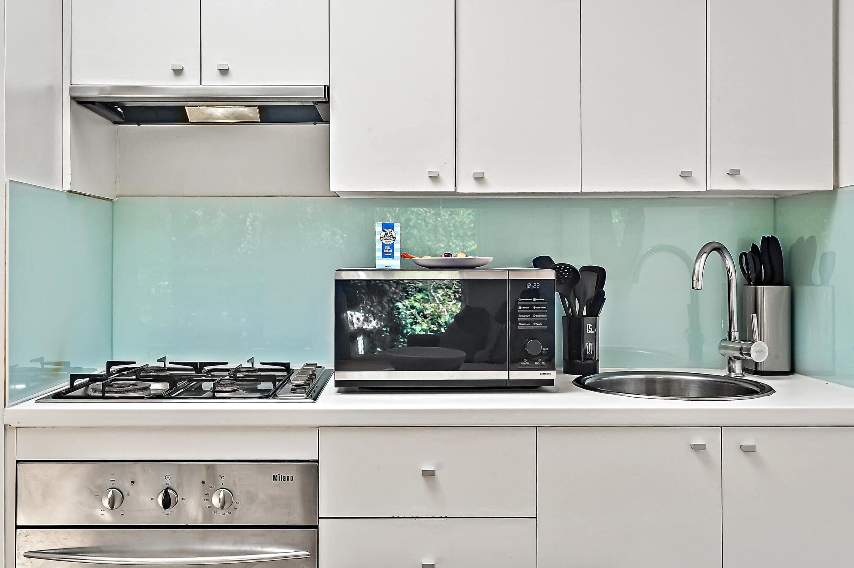 Cozinha moderna com fogão a gás, micro-ondas, pia e armários brancos.