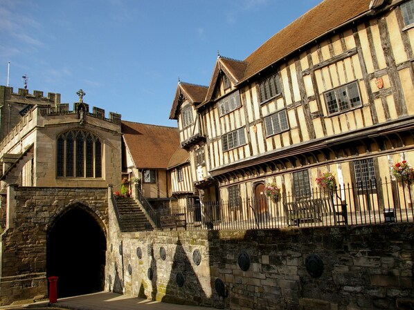 A historic building with a stone archway entrance, a staircase leading to the upper floor, and a mix of timber framing and stone construction. - 3 Leycester Court (Warwick)