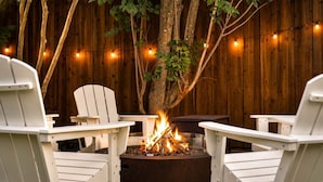 A backyard with a fire pit, two white Adirondack chairs, and a wooden fence.