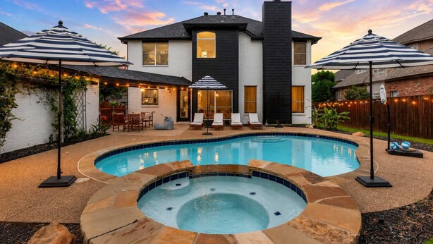 A two-story house with a swimming pool, hot tub, and outdoor seating area with umbrellas.