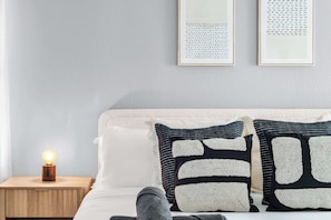 Camera da letto ordinata con un letto, cuscini, una lampada da comodino e due quadri appesi alla parete.