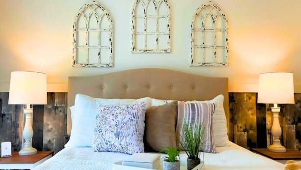 Quarto com uma cama grande, arandelas decorativas e três janelas em arco.