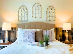 Een slaapkamer met een groot bed, decoratieve wandlampen en drie boogvensters.