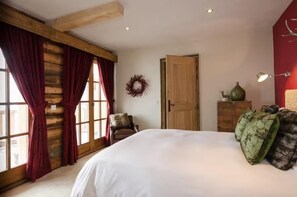 Ein Schlafzimmer mit einem großen Bett, Holzbalken, einer Holztür, einem Stuhl, einer Kommode und einer Wandlampe.