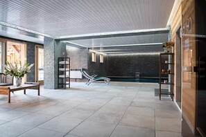 Ein moderner, überdachter Poolbereich mit Glasdecke, einer Sitzecke mit Tisch und Stühlen sowie einem Regal mit Dekorationsgegenständen.