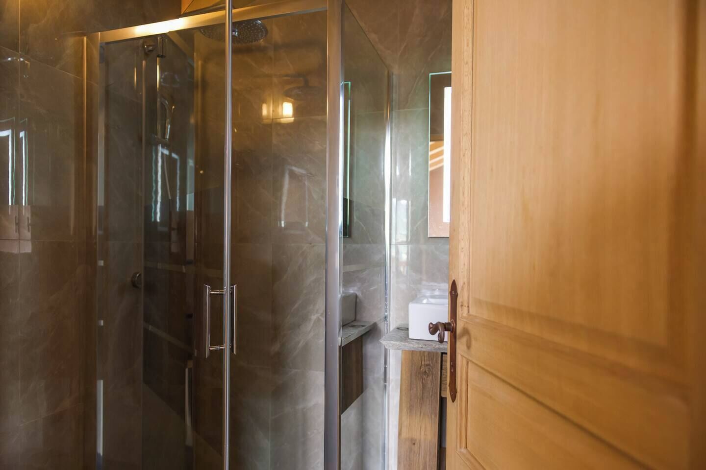 A bathroom with a glass shower enclosure, a wooden door, and a white sink.