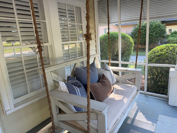 A porch with a swing seat, white shutters, and a view of greenery.