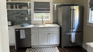A kitchen with white cabinets, a stainless steel refrigerator, a window with a gray blind, and a hanging light fixture. - Quaint cottage walk to Historic downtown, restaurants and Silver Comet Trail (Powder Springs)