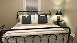 A bed with a metal frame, white bedding, and two dark pillows. There is a small table with a lamp beside the bed. - Quaint cottage walk to Historic downtown, restaurants and Silver Comet Trail (Powder Springs)