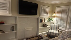 A living room with a large flat-screen TV mounted on the wall, a striped armchair, a sofa with floral cushions, and a fireplace with a mantel. - Quaint cottage walk to Historic downtown, restaurants and Silver Comet Trail (Powder Springs)