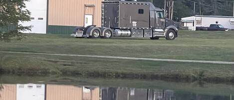 A large truck parked near a building with a reflection in a body of water.