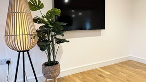 Une pièce dotée d’un plancher en bois, d’une grande plante en pot, d’un grand lampadaire et d’un téléviseur à écran plat fixé au mur.