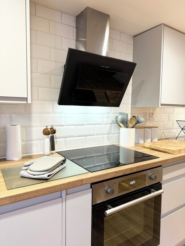A modern kitchen with a black induction cooktop, stainless steel oven, and white cabinetry.