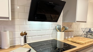 Une cuisine moderne dotée d’une plaque de cuisson à induction noire, d’un crédence carrelée blanche, d’un plan de travail en bois et d’une hotte en acier inoxydable.