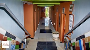 Een hotelgang met oranje wanden, een groen plafond en een betegelde vloer. Er hangen afbeeldingen in lijsten aan de muur en in het midden staat een potplant.