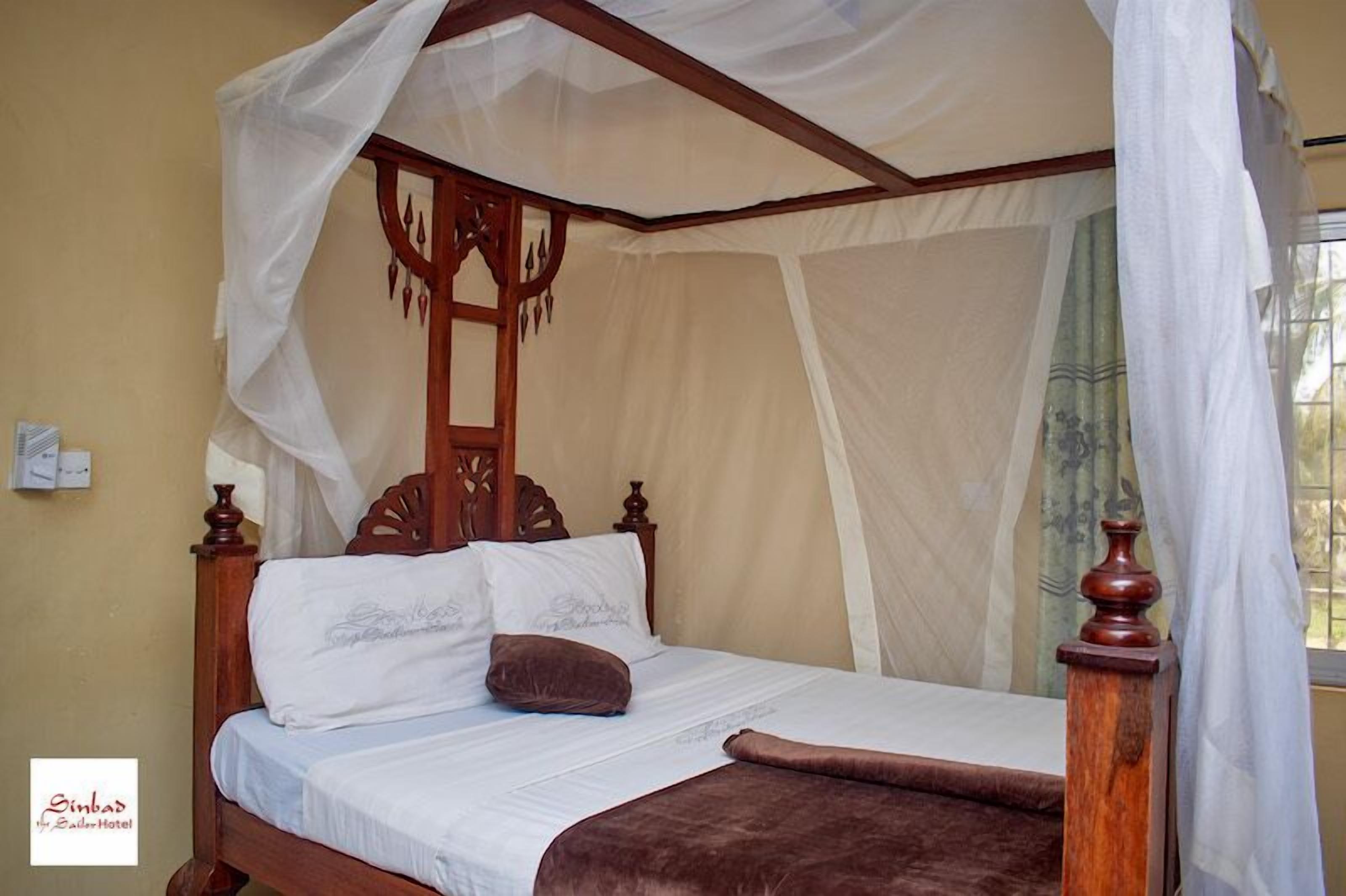 Een hemelbed met een baldakijn, witte lakens en een bruine plaid.
