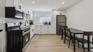 Una cucina moderna con mobili bianchi, un forno nero, un frigorifero in acciaio inossidabile e un tavolo da pranzo in legno con sedie.