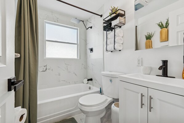 A modern bathroom with a bathtub, toilet, and a window. - Elite Stay Partners- Largo (Largo)