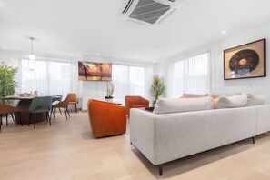 Ein modernes Wohnzimmer mit grauem Sofa, orangefarbenem Sessel und einem Essbereich mit Tisch und Stühlen.
