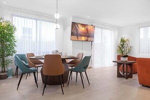 A modern living room with a dining area, featuring a round table, teal and brown chairs, a large painting, and a potted plant. - NOK Elegant 3BR Retreat with Private Pool (Punta Cana)